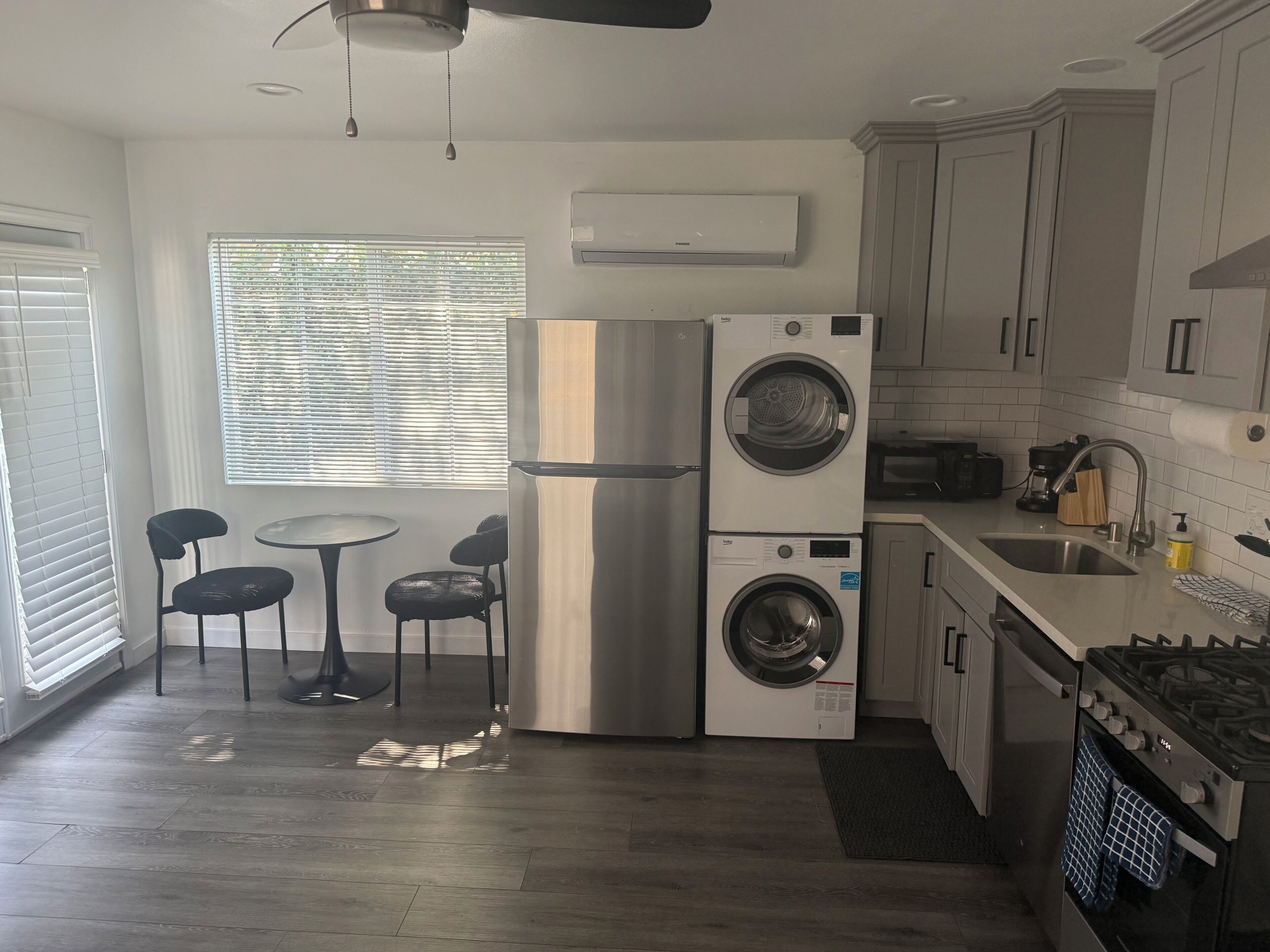 A compact kitchen with a built-in washer and dryer, a dining area with two chairs, and a window with blinds.