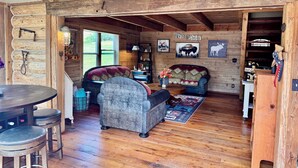 Een rustiek houten interieur met een houten plafond, een bank, een eettafel en een bar.