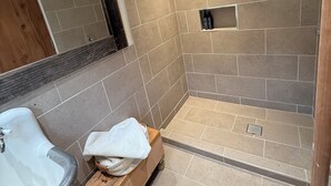 Een moderne badkamer met een douche, een houten bankje en een plank met toiletartikelen.