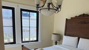 Een slaapkamer met een houten bed, een kroonluchter, een raam met potplanten en een nachtkastje met een lamp.