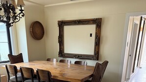 Een eetruimte met een grote houten tafel, zes stoelen, een kroonluchter en een spiegel aan de muur.
