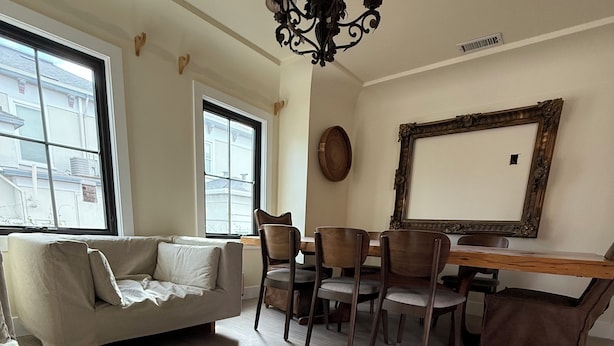 Een woonkamer met een bank, eettafel, stoelen, een kroonluchter en een grote spiegel.