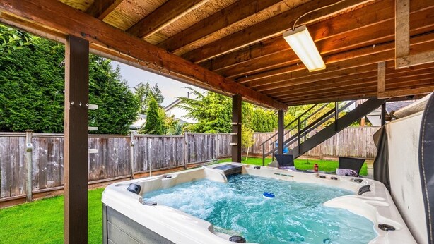 Un jacuzzi bajo una pérgola de madera, con una valla de madera al fondo.
