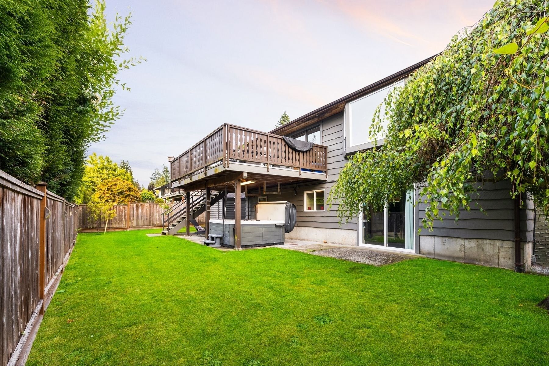 A backyard with a wooden deck, a covered barbecue area, and a house with a grey exterior.