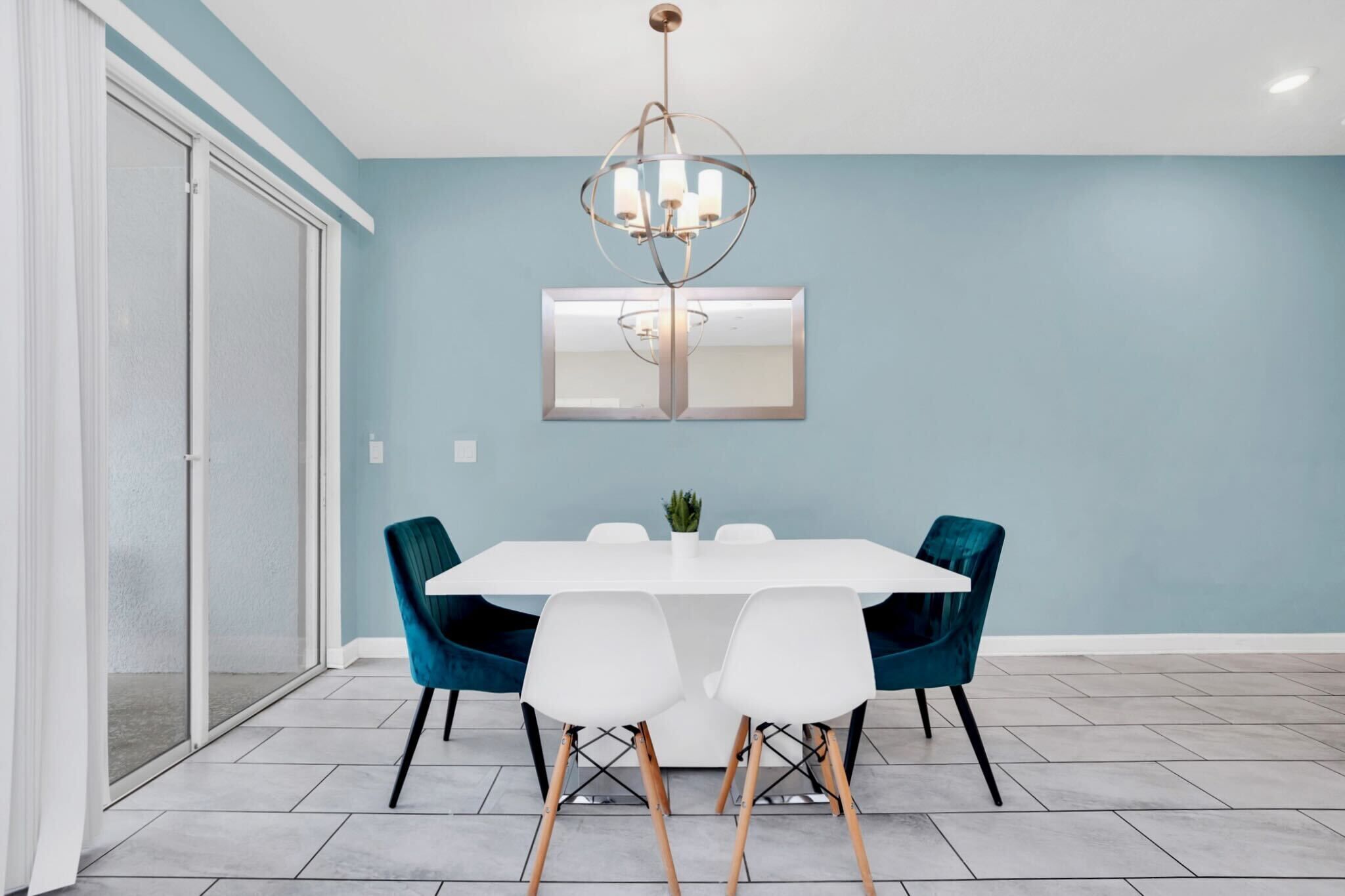 A dining area with a white table, teal chairs, and a chandelier.