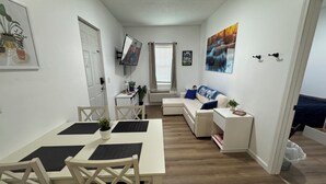 Un espacio habitable compacto con comedor, sofá, televisor y ventana con cortinas.