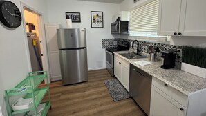 Una cocina con armarios blancos, un refrigerador de acero inoxidable, un microondas y un lavaplatos.