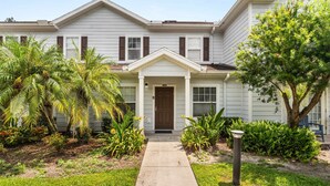 A two-story house with a front porch, a mailbox, and a well-maintained garden with various plants and a palm tree. - Upstay Modern 3BR Townhome With Pool Near Disney (Kissimmee)