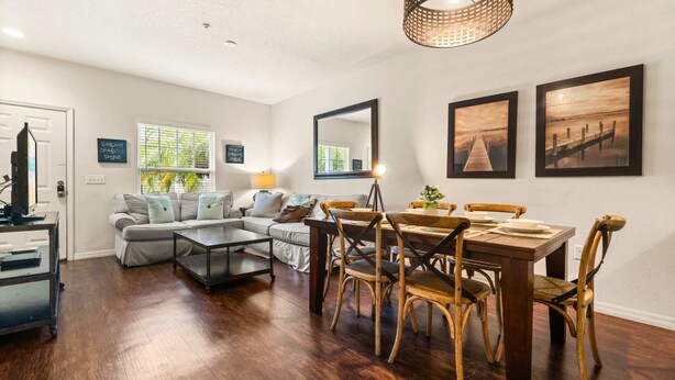 A living room with a sofa, coffee table, dining table with chairs, a TV, and artwork on the walls. - Upstay Modern 3BR Townhome With Pool Near Disney (Kissimmee)