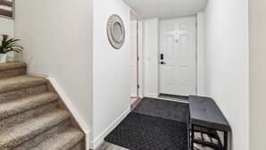 A hallway with a carpeted staircase, a door, and a small table with a bench. - Charming Basement Suite With Parking & Laundry (Calgary)