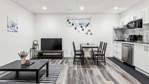 A compact living space with a dining area, a TV, and a kitchenette. - Charming Basement Suite With Parking & Laundry (Calgary)