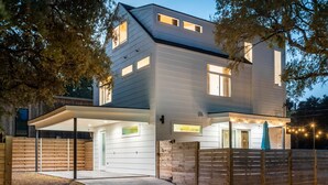A modern two-story house with a covered patio, a garage, and a wooden fence. - Stylish Eastside Getaway w Backyard, Firepit & BBQ (Austin)