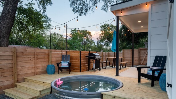 A backyard with a hot tub, wooden deck, outdoor seating, and a covered patio area. - Stylish Eastside Getaway w Backyard, Firepit & BBQ (Austin)