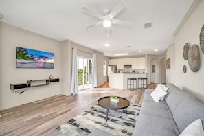 A modern living room with a grey sofa, a round coffee table, and a flat-screen TV mounted on the wall. - Upstay Pet Friendly Condo 6 Minutes From Disney (Winter Garden)