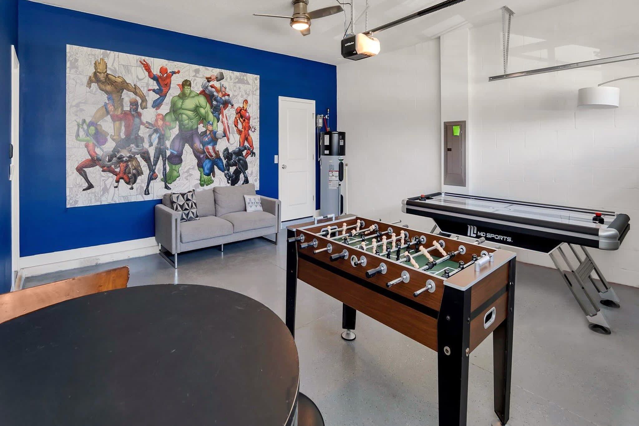 A room with a foosball table, a sofa, and a large superhero-themed mural on the wall.