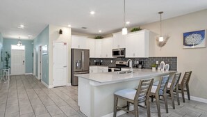 A modern kitchen with white cabinets, a large island with bar stools, stainless steel appliances, and a backsplash of dark tiles. - 8BR Luxury Sleeps 22 w Pool & Hot Tubnear Disney (Davenport)