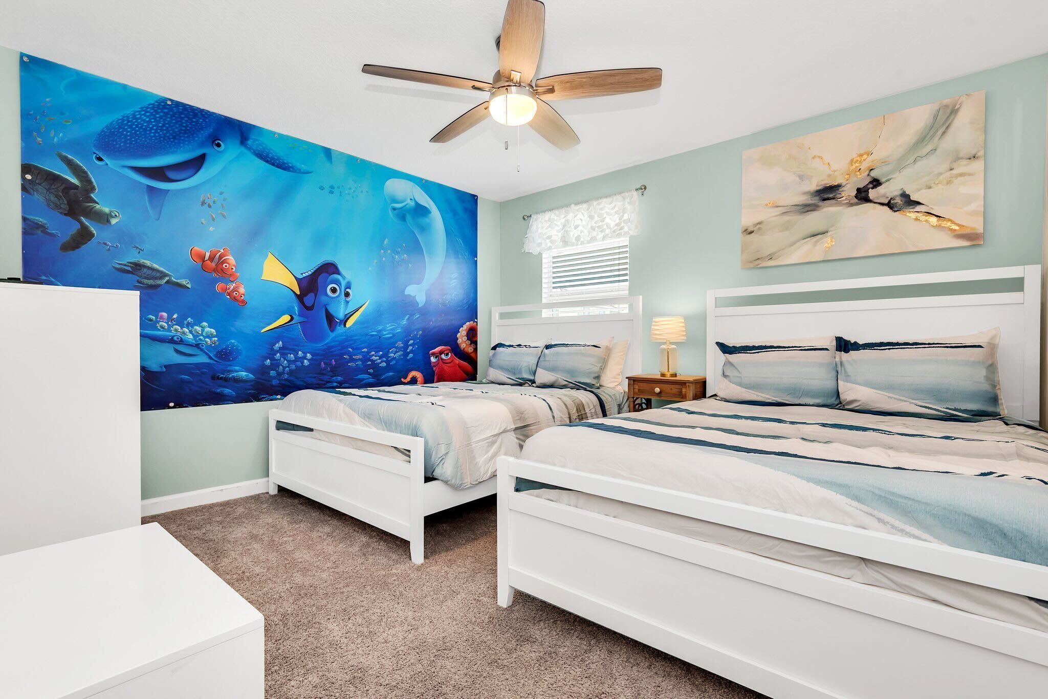 Een slaapkamer met twee witte bedden, een plafondventilator, een groot muurschildering van zeedieren en een raam met zonwering.