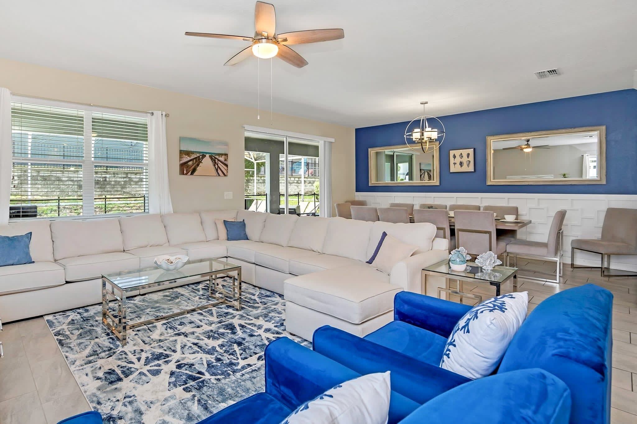 A modern living room with a sectional sofa, a blue armchair, a glass coffee table, and a ceiling fan.