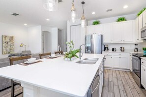 A modern kitchen with white cabinets, stainless steel appliances, and a central island with a sink and seating. - Upstay: Luxury 10br Mansion w Pool,hot Tub & Games (Kissimmee)
