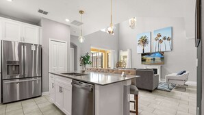 A modern kitchen with stainless steel appliances, a central island, and a seating area with a sofa and armchairs. - Upstay Modern 5BR Resort Home w Pool & Hot Tub (Kissimmee)