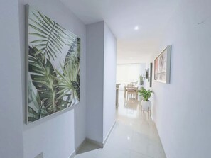 A hallway with a large tropical leaf painting, a dining area with chairs and a table, and a potted plant.