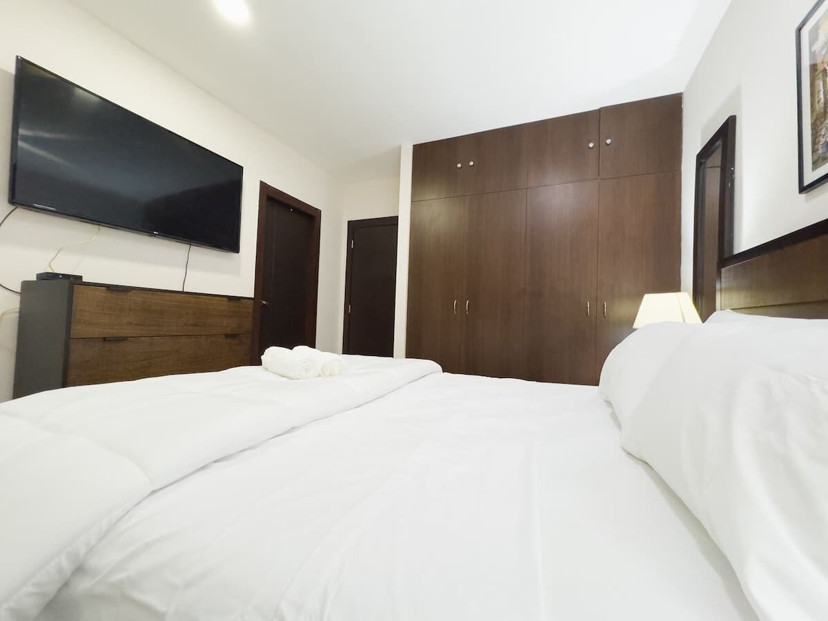 Hotellihuone, jossa on suuri sänky, seinälle asennettu taulutelevisio ja useita ovia sisältävä vaatekaappi.