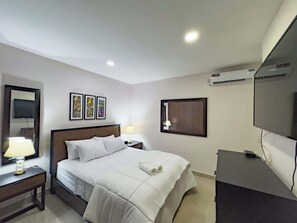 Ein Hotelzimmer mit einem Bett, Nachttischen, einem Fernseher und gerahmten Kunstwerken an den Wänden.