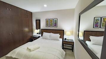 Habitación de hotel con una cama grande, un armario, una mesita de noche con lámpara y un espejo que refleja la cama.