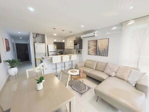 A modern living room with a sofa, a dining table, and a kitchen in the background.