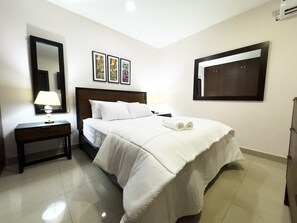 Une chambre d’hôtel avec un lit, une table de chevet, une lampe, un miroir fixé au mur et des tableaux encadrés.
