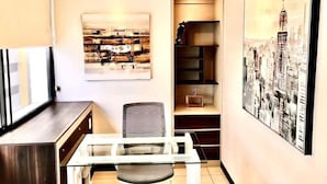 Una habitación moderna con una mesa de vidrio, una silla, un sofá, una estantería y dos obras de arte enmarcadas.