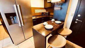Una cocina moderna con refrigerador de acero inoxidable, cafetera integrada, un lavamanos y una pequeña isla con taburetes.