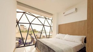 Une chambre à coucher avec un lit, une fenêtre donnant sur un paysage aux formes géométriques et un appareil de climatisation.