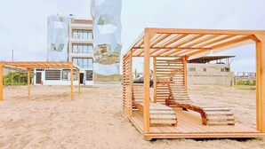 Une plage avec des chaises longues en bois et un bâtiment moderne à la façade géométrique.