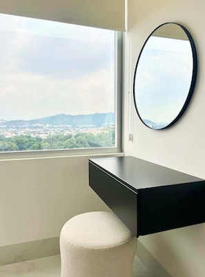 Ein modernes Badezimmer mit großem Fenster, rundem Spiegel, schwarzem Waschtisch und weißem Hocker.