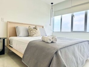 Ein modernes Schlafzimmer mit Bett, Kissen, Nachttisch und Fenster mit Blick.