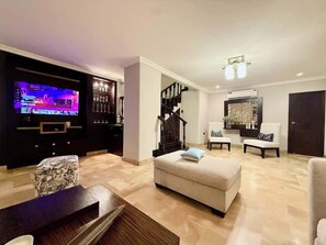 A living room with a flat-screen TV, a staircase, a dining area, and a seating area with chairs and a sofa. - Large Apt in Lomas Urdesa • Sleeps 8 • BBQ (Guayaquil)
