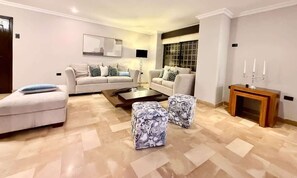 A living room with a sofa set, two ottomans, a coffee table, and a side table with candles. - Large Apt in Lomas Urdesa • Sleeps 8 • BBQ (Guayaquil)
