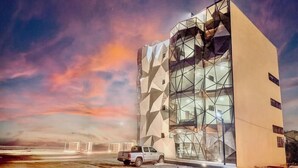 A modern building with geometric facade, a truck parked in front, and a sunset sky. - Beachfront, pool, whirlpool & firepit (Montanita)