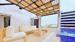 A modern outdoor living area with a wooden pergola, a white sofa, a wooden coffee table, and a pool with blue mosaic tiles. - Beachfront, pool, whirlpool & firepit (Montanita)