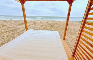 A beach hut with a bed, wooden slats, and a view of the ocean.