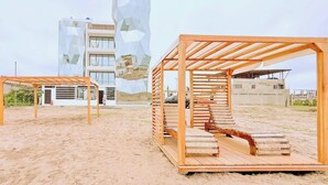 A beach with wooden sun loungers and a modern building with geometric design in the background.