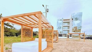 A beachside hotel with wooden cabanas, a modern building with geometric facade, and a clear sky.
