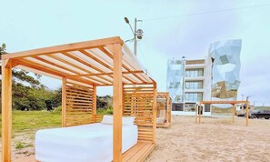 A beachside hotel with wooden cabanas, a modern building with geometric facade, and a clear sky.