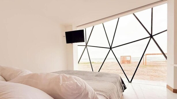 A bedroom with a bed, a TV, and a view of the beach through a geometric window design.