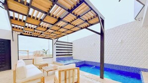 A covered outdoor area with a pool, seating, and a view of the beach.