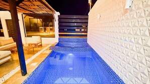 A pool area with a geometric pattern on the floor, a white wall with a textured design, and a view of the outside at night. - Oceanfront Paradise with Pool, Hot Tub and Firepit (Montanita)