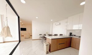 Una cocina moderna con gabinetes blancos, encimera de mármol y un comedor con sillas.