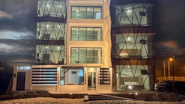 Un edificio moderno de varios pisos con fachada geométrica, ventanas amplias y una entrada bien iluminada.