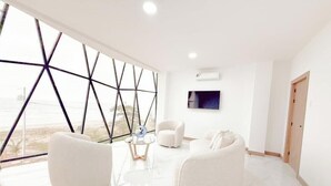 Una habitación moderna con un gran ventanal, muebles blancos y un televisor de pantalla plana.